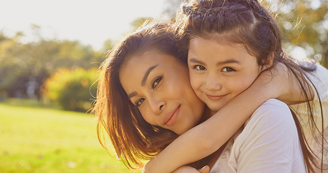 Little girl hugging her mom in the grass on a sunny day