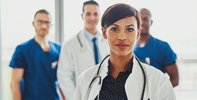 Female doctor standing in the fore-ground smiling and other doctors in the back ground