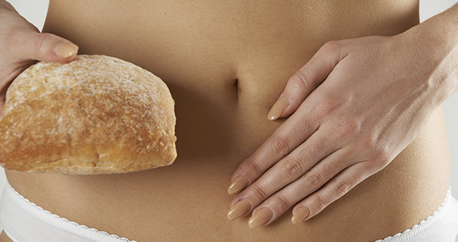 Image of a woman holding her abdominal area with one hand and bread in her other hand