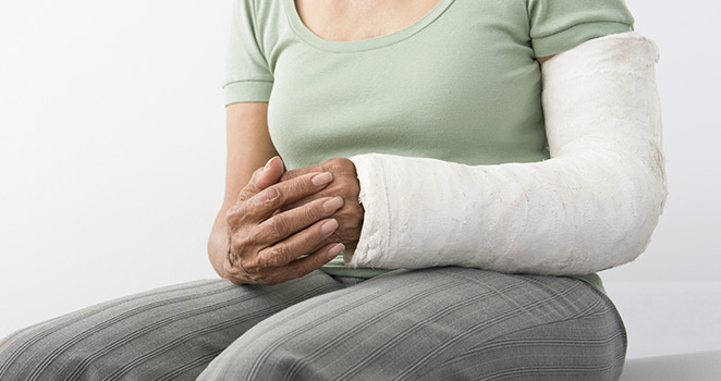 Older woman sittin on a table with a cast on her arm.