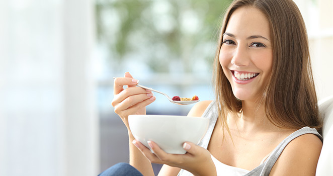 Young woman eating healthy cereal and fruit