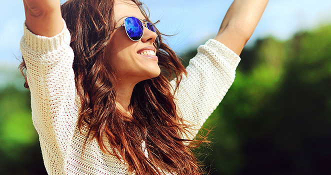 Young woman standing in the sunshine with her arms raised to the sky