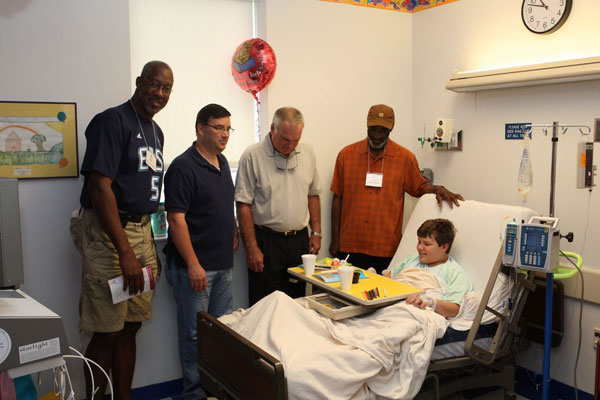 Some of the men visit a young patient in his hospital room