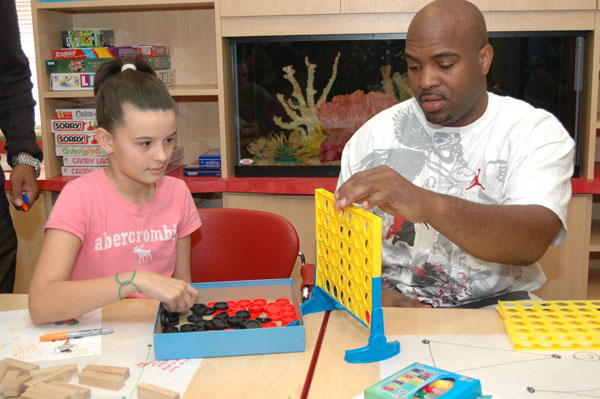 A man plays connect four with a young girl