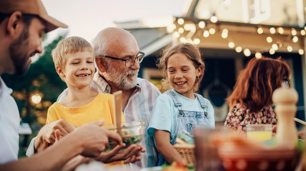 older man sitting with two children in his lap at a table outside