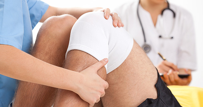 Doctor examining a man's knee that has a brace on it