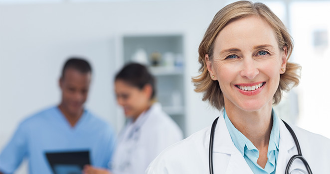 Female doctor standing in the fore-ground smiling and other doctors in the back ground